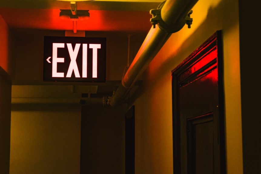 An exit sign illuminated in red color hangs from the ceiling